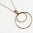 Double Happiness Bronze Circle Pendant Necklace - shown laying on a white background. The two handmade, hammered, concentric circles on a rose gold chain reflect with lovely contrasting warm bronze tones. The two nested circles rustic look is complimented by the hypoallergenic gold fill chain and handmade wire wrapped clasp. Together, the Double Happiness Bronze Circles Pendant Necklace is a simple necklace to wear everyday, or on the best of occasions. Bronze 8th anniversary gifts for her