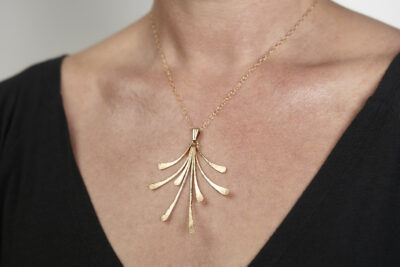 The Flash - Bronze Statement Necklace worm on a woman wearing a black sweater, Featuring 8 gently curving dangling bronze elements hammered and faceted to reflect the light. The Flash - Bronze Statement Necklace is a beautifully understated yet striking statement necklace. The hammered bronze reflects the warm light in facets creating a lovely 8th anniversary gift for her. The gold fill chain matches the warm tones of the bronze perfectly. Light enough for every day, but sophisticated enough for a fancy night out, The Flash - Bronze Statement Necklace are a perfect gift for any occasion. Bronze 8th anniversary gifts