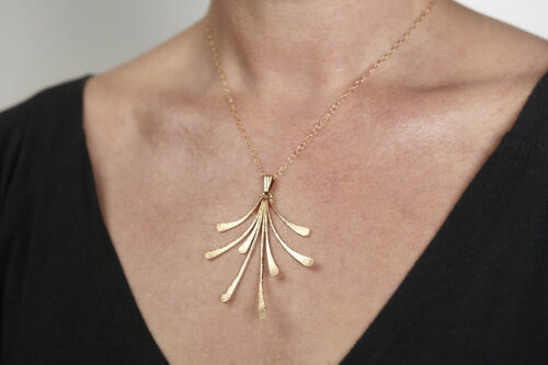 The Flash - Bronze Statement Necklace worm on a woman wearing a black sweater, Featuring 8 gently curving dangling bronze elements hammered and faceted to reflect the light. The Flash - Bronze Statement Necklace is a beautifully understated yet striking statement necklace. The hammered bronze reflects the warm light in facets creating a lovely 8th anniversary gift for her. The gold fill chain matches the warm tones of the bronze perfectly. Light enough for every day, but sophisticated enough for a fancy night out, The Flash - Bronze Statement Necklace are a perfect gift for any occasion. Bronze 8th anniversary gifts