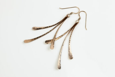 The Mini Flash - bronze drop earrings displayed laying on a white background, Featuring 3 gently curving dangling bronze elements hammered and faceted to reflect the light. The Mini Flash - bronze drop earrings are a beautifully understated yet striking pair of statement earrings. The hammered bronze reflects the warm light in facets creating a lovely 8th anniversary gift for her. The gold fill chain matches the warm tones of the bronze perfectly. Light enough for every day, but sophisticated enough for a fancy night out, The mini Flash - bronze drop earrings are a perfect gift for any occasion. Bronze 8th anniversary gifts
