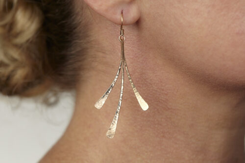 The Mini Flash - Hammered Bronze Earrings displayed laying on a white background, Featuring 3 gently curving dangling bronze elements hammered and faceted to reflect the light. The Mini Flash - Hammered Bronze Earrings are a beautifully understated yet striking pair of statement earrings. The hammered bronze reflects the warm light in facets creating a lovely 8th anniversary gift for her. The gold fill chain matches the warm tones of the bronze perfectly. Light enough for every day, but sophisticated enough for a fancy night out, The mini Flash - Hammered Bronze Earrings are a perfect gift for any occasion. Bronze 8th anniversary gifts