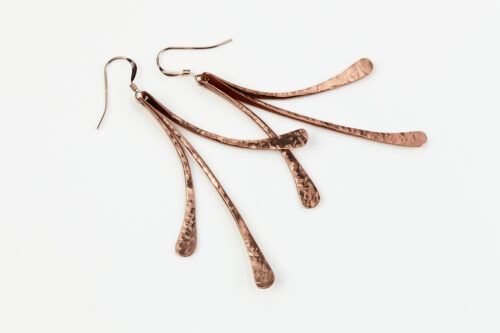 7th anniversary Mini Flash - Copper drop earrings displayed laying on a white background. The three gently curved, hammered copper elements display their unique faceted texture in the warm light. Copper 7th anniversary gifts for wife