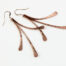 7th anniversary Mini Flash - Copper drop earrings displayed laying on a white background. The three gently curved, hammered copper elements display their unique faceted texture in the warm light. Copper 7th anniversary gifts for wife