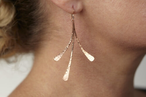 Dirtypretty artwear's Mini Flash Hammered Copper Earrings shown on a model. The three gently curved, hand hammered copper elements shine in the warm light. Copper 7th anniversary gifts for wife