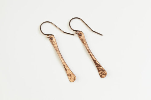 Simple Chic - Dainty Copper earrings displayed laying on a white background. The uniquely minimalist copper bar dangle earrings, display their uniquely hammered textures in the warm light. Rose gold filled ear wires match the warm tones of the copper. Copper gifts for wife