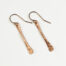 Simple Chic - Dainty Copper earrings displayed laying on a white background. The uniquely minimalist copper bar dangle earrings, display their uniquely hammered textures in the warm light. Rose gold filled ear wires match the warm tones of the copper. Copper gifts for wife