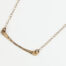 Simple Chic - Bronze Bar Pendant displayed laying on a white background. The uniquely minimalist Bronze curved bar necklace displays its hand forged textures in the warm light. The gold filled chain matches the warm tones of the Bronze showcasing its simple elegance. 8th anniversary gifts
