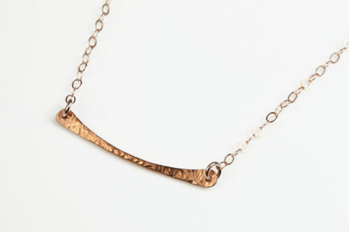 Simple Chic - Horizontal Bar Necklace displayed laying on a white background. The uniquely minimalist copper horizontal bar necklace displays its hand forged textures in the warm light. Rose gold filled chain matches the warm tones of the copper showcasing its simple elegance. Copper anniversary gifts for her