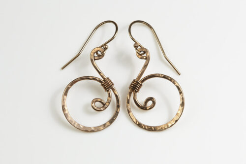 Tiny Swirls - Bronze Spiral Earrings displayed laying on a white background. These bronze drop hoop earrings have a wire wrapped bronze detail that creates the closed circle of the hoops with a tiny spiral inside the hoop to provide the cute focal point of the earrings. Delicately hammered facets reflect the light of the bronze. The gold fill ear wires match the warm tones of the Bronze perfectly. Small and light enough for every day, but sophisticated enough for a fancy night out, the Tiny Swirls - Bronze Spiral Earrings are perfect for every occasion. Bronze 8th anniversary gifts for her