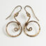 Tiny Swirls - Bronze Spiral Earrings displayed laying on a white background. These bronze drop hoop earrings have a wire wrapped bronze detail that creates the closed circle of the hoops with a tiny spiral inside the hoop to provide the cute focal point of the earrings. Delicately hammered facets reflect the light of the bronze. The gold fill ear wires match the warm tones of the Bronze perfectly. Small and light enough for every day, but sophisticated enough for a fancy night out, the Tiny Swirls - Bronze Spiral Earrings are perfect for every occasion. Bronze 8th anniversary gifts for her