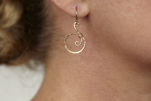 Tiny Swirls - Bronze Spiral Earrings displayed laying on a white background. These bronze drop hoop earrings have a wire wrapped bronze detail that creates the closed circle of the hoops with a tiny spiral inside the hoop to provide the cute focal point of the earrings. Delicately hammered facets reflect the light of the bronze. The gold fill ear wires match the warm tones of the Bronze perfectly. Small and light enough for every day, but sophisticated enough for a fancy night out, the Tiny Swirls - Bronze Spiral Earrings are perfect for every occasion. Bronze 8th anniversary gifts for her