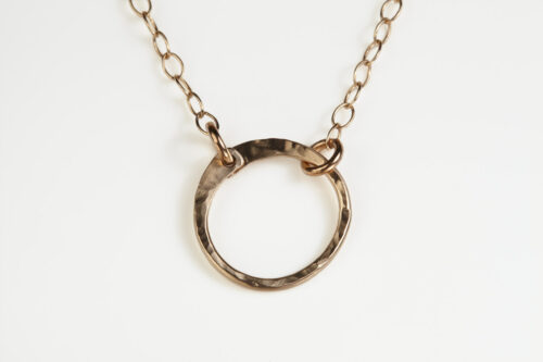 The Tiny Zen Circle - Bronze Simple Circle Necklace. Shown on a white background, a simple hammered bronze circle embodying the Japanese concept of Enso, the Tiny Zen Circle - Bronze Simple Circle Necklace a beautifully understated yet striking necklace. The hammered bronze reflects the warm light in facets creating a lovely and simple everyday necklace. The gold fill chain matches the warm tones of the bronze perfectly. Small and light enough for every day, but sophisticated enough for a fancy night out, The Tiny Zen Circle - Bronze Simple Circle Necklace is a perfect gift for every occasion and makes a lovely Bronze 8th anniversary gifts for her
