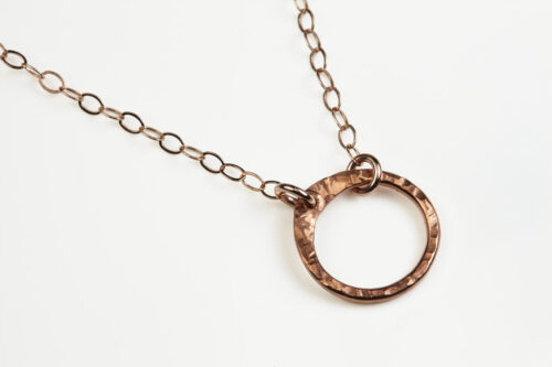The Tiny Zen Circle - Simple Copper Circle Necklace. Shown on a white background, a simple hammered copper circle embodying the Japanese concept of Enso, the Tiny Zen Circle - Simple Copper Circle Necklace a beautifully understated yet striking necklace. The hammered copper reflects the warm light in facets creating a lovely and simple everyday necklace. The rose gold fill chain matches the warm tones of the copper perfectly. Small and light enough for every day, but sophisticated enough for a fancy night out, The Tiny Zen Circle - Simple Copper Circle Necklace is a perfect gift for every occasion and makes a lovely copper 7th anniversary gift for her