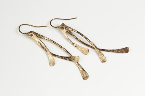Trio Elegant Dangle Earrings in Bronze displayed laying on a white background. The three delicately curved and hammered bronze dangles reflect the light in facets. The gold fill ear wires match the warm tones of the bronze perfectly. Small and light enough for every day, but sophisticated enough for a fancy night out, the Trio Dangle Earrings in Bronze are perfect for every occasion. 8th anniversary gifts for her