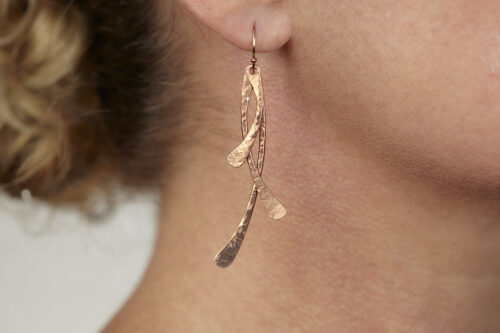 Trio Elegant Copper Earrings displayed laying on a white background. The three delicately curved and hammered copper dangles reflect the light in facets. The rose gold fill ear wires match the warm tones of the copper perfectly. Small and light enough for every day, but sophisticated enough for a fancy night out, the Trio Earrings are perfect for every occasion. Copper 7th anniversary gifts for her