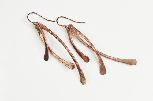 Trio Elegant Copper Earrings displayed laying on a white background. The three delicately curved and hammered copper dangles reflect the light in facets. The rose gold fill ear wires match the warm tones of the copper perfectly. Small and light enough for every day, but sophisticated enough for a fancy night out, the Trio Earrings are perfect for every occasion. Copper 7th anniversary gifts for her