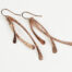 Trio Elegant Copper Earrings displayed laying on a white background. The three delicately curved and hammered copper dangles reflect the light in facets. The rose gold fill ear wires match the warm tones of the copper perfectly. Small and light enough for every day, but sophisticated enough for a fancy night out, the Trio Earrings are perfect for every occasion. Copper 7th anniversary gifts for her
