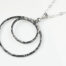 Double Happiness Aluminum Circles Necklace - shown laying on a white background. The two handmade, hammered, concentric circles on a sterling silver chain reflect with lovely contrasting aluminum tones. The two nested circles rustic look is complimented by the hypoallergenic sterling silver chain and handmade wire wrapped clasp. Together, the Double Happiness Aluminum Circles Necklace is a simple necklace to wear everyday, or perfect for a night on the town.