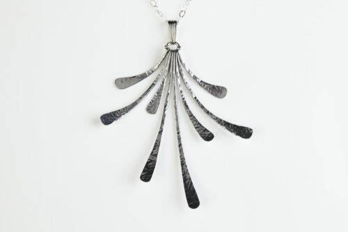 The Flash - Hammered Aluminum Necklace displayed laying on a white background, Featuring 8 gently curving dangling Aluminum elements hammered and faceted to reflect the light. The Flash - Hammered Aluminum Necklace is a beautifully understated yet striking Aluminum statement necklace. The hammered Aluminum reflects the light in facets creating a lovely 10th anniversary gift for her. The sterling silver chain matches the cool tones of the Aluminum perfectly. Light enough for every day, but sophisticated enough for a fancy night out, The Flash - Hammered Aluminum Necklace is a perfect gift for any occasion.