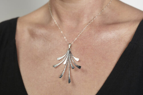 The Flash - Hammered Aluminum Necklace displayed laying on a white background, Featuring 8 gently curving dangling Aluminum elements hammered and faceted to reflect the light. The Flash - Hammered Aluminum Necklace is a beautifully understated yet striking Aluminum statement necklace. The hammered Aluminum reflects the light in facets creating a lovely 10th anniversary gift for her. The sterling silver chain matches the cool tones of the Aluminum perfectly. Light enough for every day, but sophisticated enough for a fancy night out, The Flash - Hammered Aluminum Necklace is a perfect gift for any occasion.