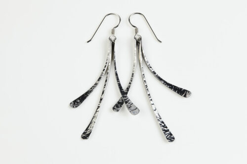 The Mini Flash - Hammered Aluminum Earrings displayed laying on a white background, Featuring 3 gently curving dangling Aluminum elements hammered and faceted to reflect the light. The Mini Flash - Hammered Aluminum Earrings are a beautifully understated yet striking pair of Aluminum statement earrings. The hammered Aluminum reflects the light in facets creating a lovely 10th anniversary gift for her. The sterling silver chain matches the hammered aluminum perfectly. Light enough for every day, but sophisticated enough for a fancy night out, The Mini Flash - Hammered Aluminum Earrings are a perfect gift for any occasion.
