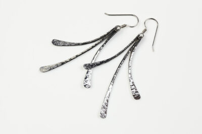 The Mini Flash - Aluminum dangle Earrings displayed laying on a white background, Featuring 3 gently curving dangling Aluminum elements hammered and faceted to reflect the light. The Mini Flash - Aluminum dangle Earrings are a beautifully understated yet striking pair of Aluminum statement earrings. The hammered Aluminum reflects the light in facets creating a lovely 10th anniversary gift for her. The sterling silver chain matches the hammered aluminum perfectly. Light enough for every day, but sophisticated enough for a fancy night out, The Mini Flash - Aluminum dangle Earrings are a perfect gift for any occasion.