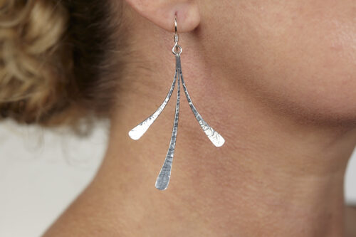The Mini Flash - Hammered Aluminum Earrings displayed laying on a white background, Featuring 3 gently curving dangling Aluminum elements hammered and faceted to reflect the light. The Mini Flash - Hammered Aluminum Earrings are a beautifully understated yet striking pair of Aluminum statement earrings. The hammered Aluminum reflects the light in facets creating a lovely 10th anniversary gift for her. The sterling silver chain matches the hammered aluminum perfectly. Light enough for every day, but sophisticated enough for a fancy night out, The Mini Flash - Hammered Aluminum Earrings are a perfect gift for any occasion.