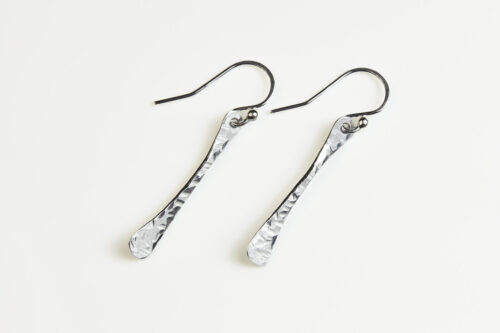 Simple Chic - Aluminum Bar earrings displayed laying on a white background. The uniquely minimalist aluminum bar dangle earrings display their uniquely hammered textures in the warm light. Sterling silver ear wires match the aluminum. These rustic and simple earrings are perfect for everyday wear, or are elegant enough for a fancy night out.