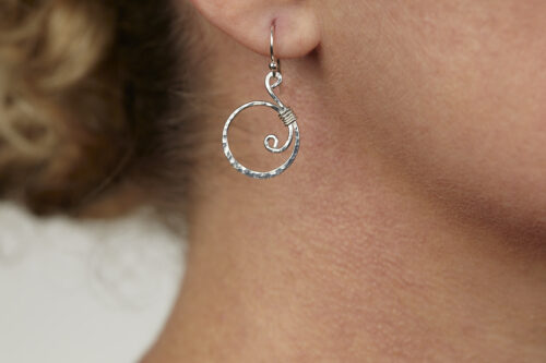 Tiny Swirls - Aluminum Spiral Earrings displayed laying on a white background. These Aluminum drop hoop earrings have a wire wrapped aluminum detail that creates the closed circle of the hoops with a tiny spiral inside the hoop to provide the cute focal point of the earrings. Delicately hammered facets reflect the light of the Aluminum. The sterling silver ear wires match the warm tones of the Aluminum perfectly. Small and light enough for every day, but sophisticated enough for a fancy night out, the Tiny Swirls - Aluminum Spiral Earrings are perfect for every occasion.