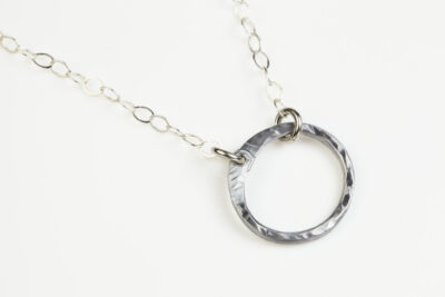 The Tiny Zen Circle - Aluminum Simple Circle Necklace. Shown on a white background, a simple hammered Aluminum circle embodying the Japanese concept of Enso, the Tiny Zen Circle - Aluminum Simple Circle Necklace a beautifully understated yet striking minimalist necklace. The hammered Aluminum reflects the cool light in facets creating a lovely and simple everyday necklace. The sterling silver chain matches the aluminum perfectly. Small and light enough for every day, but sophisticated enough for a fancy night out, The Tiny Zen Circle - Aluminum Simple Circle Necklace is a perfect gift for every occasion and makes a lovely Aluminum anniversary gift for her