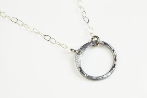 The Tiny Zen Circle - Aluminum Simple Circle Necklace. Shown on a white background, a simple hammered Aluminum circle embodying the Japanese concept of Enso, the Tiny Zen Circle - Aluminum Simple Circle Necklace a beautifully understated yet striking minimalist necklace. The hammered Aluminum reflects the cool light in facets creating a lovely and simple everyday necklace. The sterling silver chain matches the aluminum perfectly. Small and light enough for every day, but sophisticated enough for a fancy night out, The Tiny Zen Circle - Aluminum Simple Circle Necklace is a perfect gift for every occasion and makes a lovely Aluminum anniversary gift for her