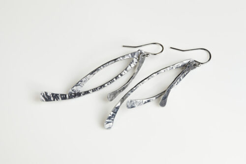 Trio Aluminum Boho Earrings displayed laying on a white background. The three delicately curved and hammered aluminum dangles reflect the light in facets. The sterling silver ear wires match the cool tones of the aluminum perfectly. Small and light enough for every day, but sophisticated enough for a fancy night out, the Trio Aluminum Boho Earrings are perfect for every occasion.