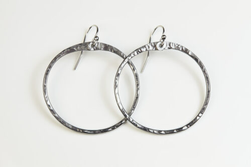 The Zen Circle - Aluminum Large Hoop Earrings. Displayed on a white background, Feature simple hammered Aluminum circles embodying the Japanese concept of Enso, the Zen Circle - Aluminum hammered hoop earrings are beautifully understated yet striking earrings. The hammered Aluminum reflects the cool light in facets creating lovely and simple everyday earrings. The sterling silver ear wires match the warm tones of the Aluminum perfectly. Small and light enough for every day, but sophisticated enough for a fancy night out, The Zen Circle - Aluminum Large Hoop Earrings are a perfect gift for any occasion.