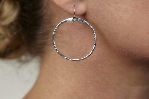 The Zen Circle - Aluminum Large Hoop Earrings. Displayed on a white background, Feature simple hammered Aluminum circles embodying the Japanese concept of Enso, the Zen Circle - Aluminum hammered hoop earrings are beautifully understated yet striking earrings. The hammered Aluminum reflects the cool light in facets creating lovely and simple everyday earrings. The sterling silver ear wires match the warm tones of the Aluminum perfectly. Small and light enough for every day, but sophisticated enough for a fancy night out, The Zen Circle - Aluminum Large Hoop Earrings are a perfect gift for any occasion.