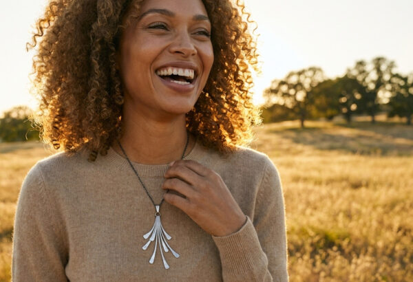 A smiling woman in the golden hour looks over a grassland holding her iron flash necklace anniversary gift for her