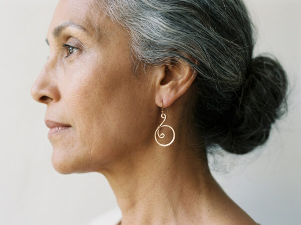 A closeup side view of a lovely woman in her 60's wearing the bronze tiny swirls earrings she received for her 8th anniversary
