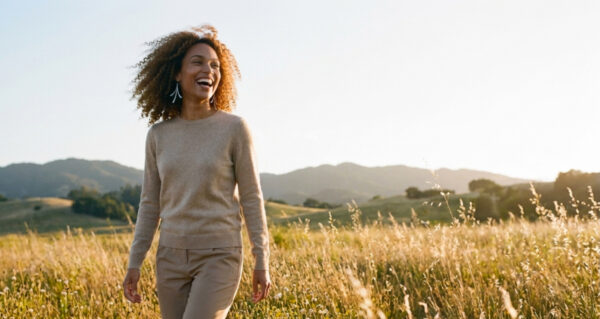 A smiling woman in the golden hour looks over a grassland holding her iron flash necklace anniversary gift for her